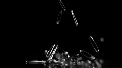 Many safety pins crashing to floor on black background - Powered by Adobe