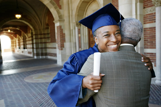 Smiling Black woman holding graduation diploma and hugging husband