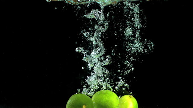 Three limes falling into water in slow motion
