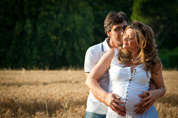 Husband embracing pregnant wife in a wheat field.