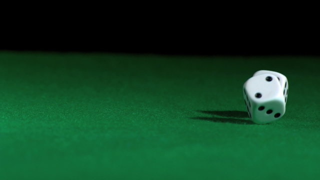 White dice rolling across green surface in slow motion