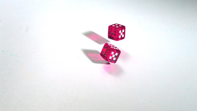 Pink dice rolling across white surface in slow motion
