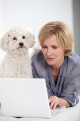 Woman on laptop computer accompanied by small white dog