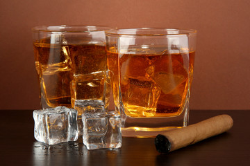 Glasses of whiskey and cigar on brown background
