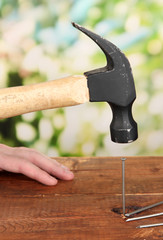 Builder hammering nails into board on natural background