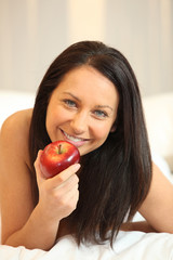 Naked woman eating an apple in bed