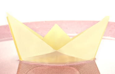 Color paper ship in water on pink plate, close-up