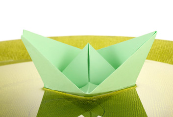 Color paper ship in water on green plate, close-up