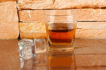 Glass of whiskey and ice on brick wall background