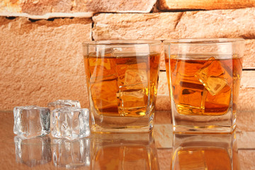Glasses of whiskey and ice on brick wall background