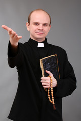 Young pastor with rosary and  Bible, on gray background