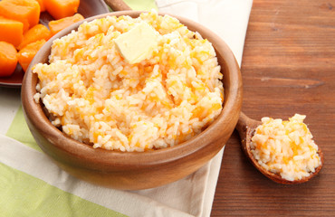 Taste rice porridge with pumpkin in bowl on wooden background.