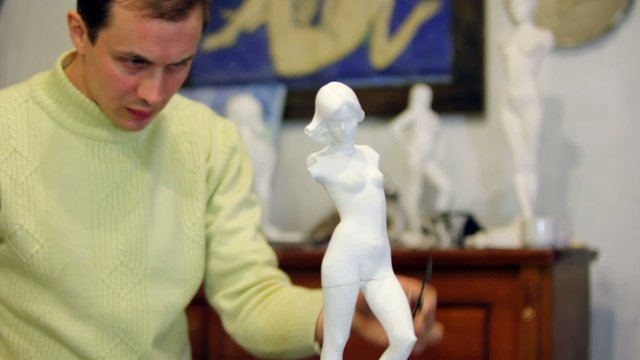 Sculptor polishes female figurine by file at background of other