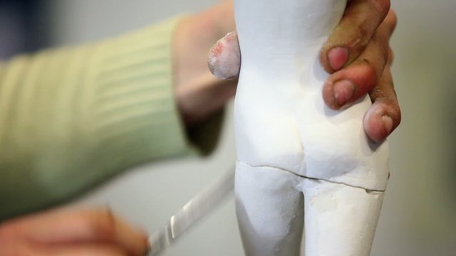 Sculptor holds female figurine and polishes its legs by file