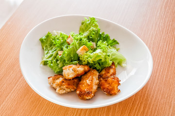 Fototapeta premium A simple white ceramic plate of chicken with some green salad leaves on a wooden table