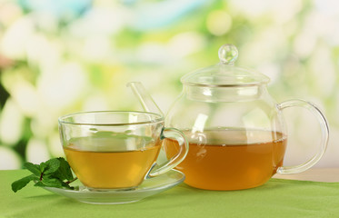 Cup of tea with mint on table on bright bacground
