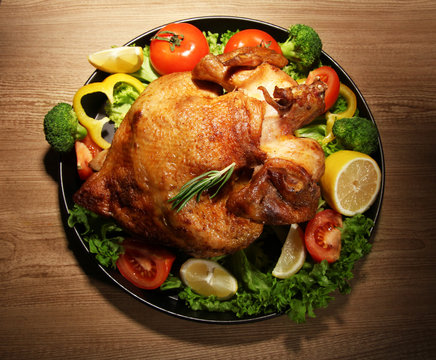 Whole roasted chicken with vegetables on plate, on wooden table
