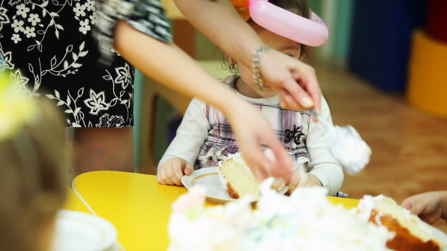 child-minder lays out pieces of cake to kids sitting at table in