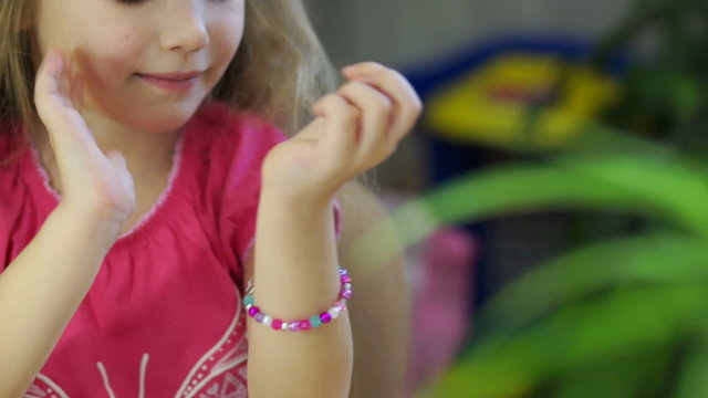 Child making jewelry from beads. Looking at camera