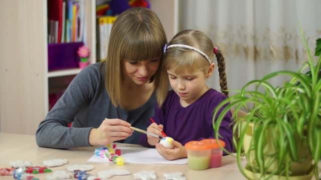 Mother and child decorate an Easter egg. Looking at camera