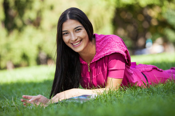 Cheerful young girl lying on grass in park, reading magazine