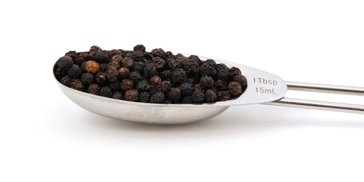 Black peppercorns measured in a metal tablespoon