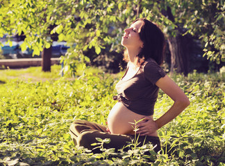 Naklejka na ściany i meble Pregnant woman relaxing on grass.