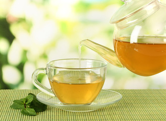 Cup of tea with mint on table on bright bacground