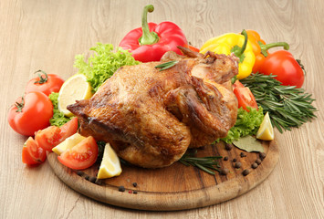 Whole roasted chicken with vegetables on plate, on wooden table