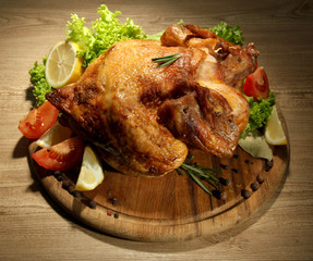 Whole roasted chicken with vegetables on plate, on wooden table