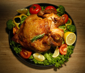 Whole roasted chicken with vegetables on plate, on wooden table