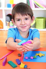 Cute little boy holding plasticine over desk