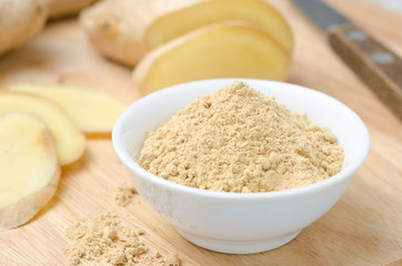 ground ginger in white bowl on a wooden board closeup