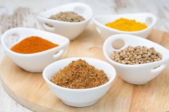 collection of spices in white bowls on the wooden board