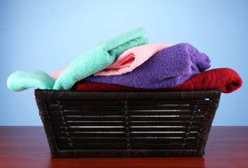 Colorful towels in basket on color background