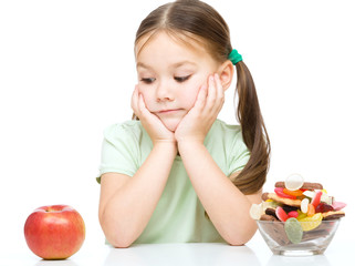 Little girl choosing between apples and sweets