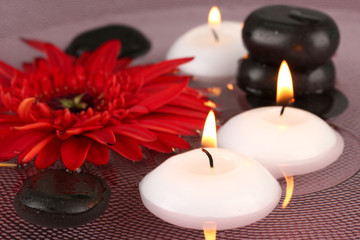 spa stones with flower and candles in water on plate