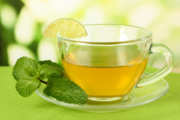 Cup of tea with mint on table on bright background