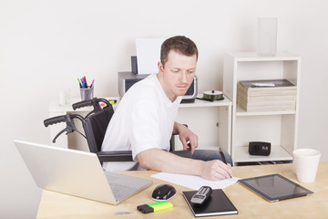 Man in wheelchair with tablet computer and laptop