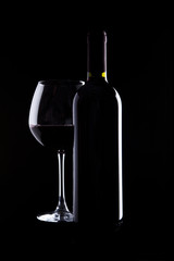 elegant glass and bottle of red wine on black background