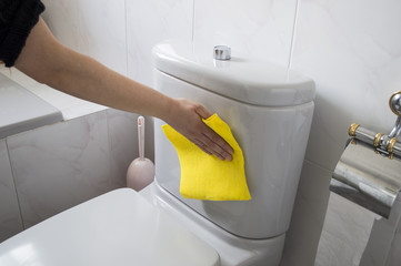 A woman cleans a toilet with yellow cloth