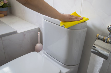 A woman cleans a toilet with yellow cloth