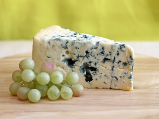 Slice of blue cheese with grapes on green background, close-up
