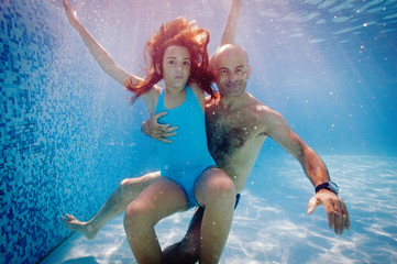 Father and daughter having fun underwater in swimming pool.