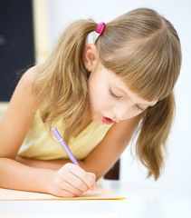 Little girl is writing using a pen