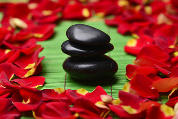 black stones with many red rose petal on a green mat