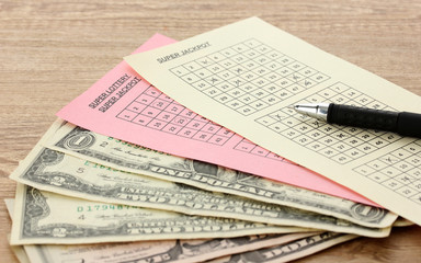 Lottery tickets with pen and money, on wooden background