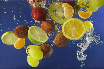 Foto op Canvas Vruchten spatten in water met bubbels tegen blauwe achtergrond © udra11