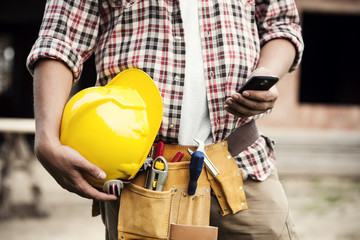 Close-up of construction worker texting on mobile phone - obrazy, fototapety, plakaty