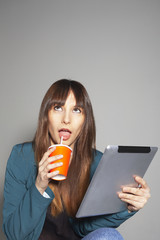 Woman looking up and drinking refreshment with digital tablet
